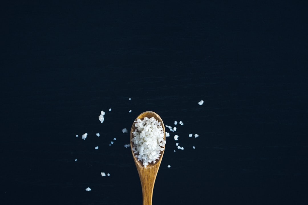 Wooden spoon holds coarse salt on a dark surface.